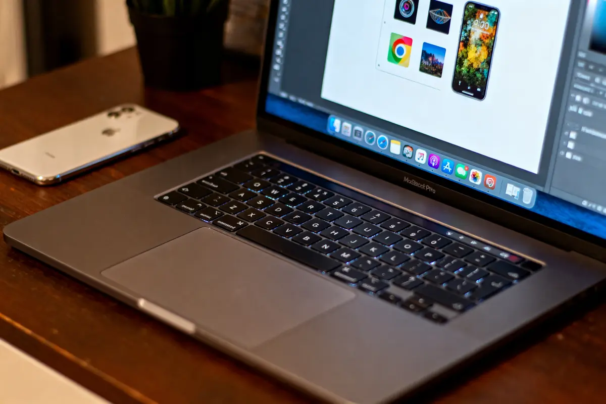 Ordinateur portable MacBook Pro ouvert sur une table en bois, smartphone à côté, applications affichées à l'écran.
